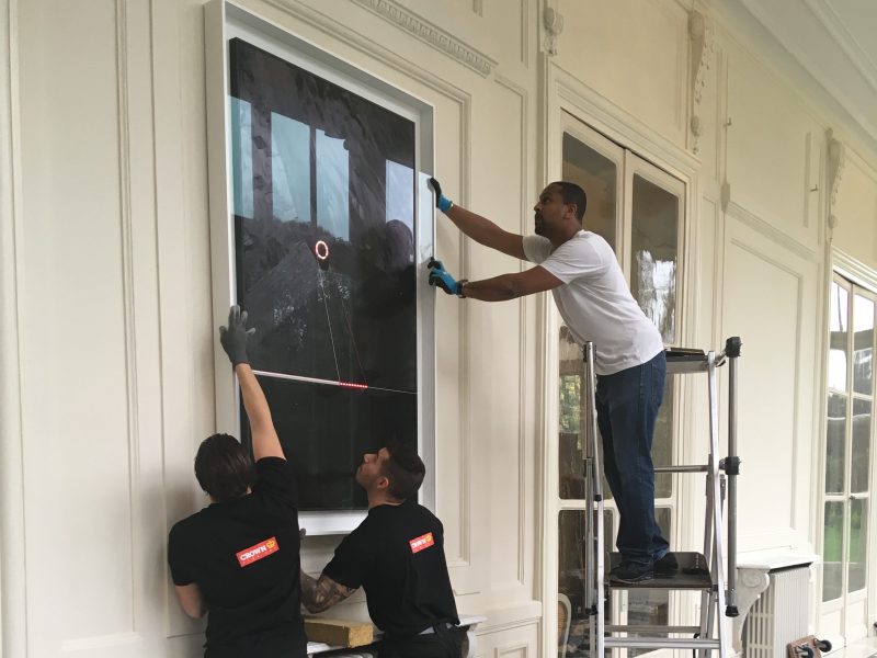 Three art technicians installing a picture on to a wall at the Ambassador's Residence in Paris