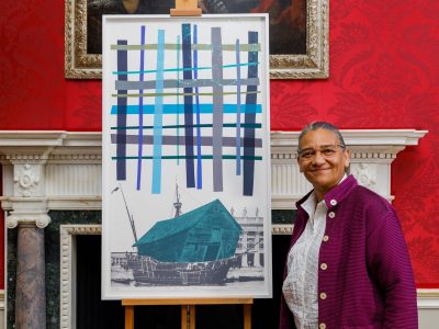 Lubaina Himid standing in from of her TenTen print against a red wall