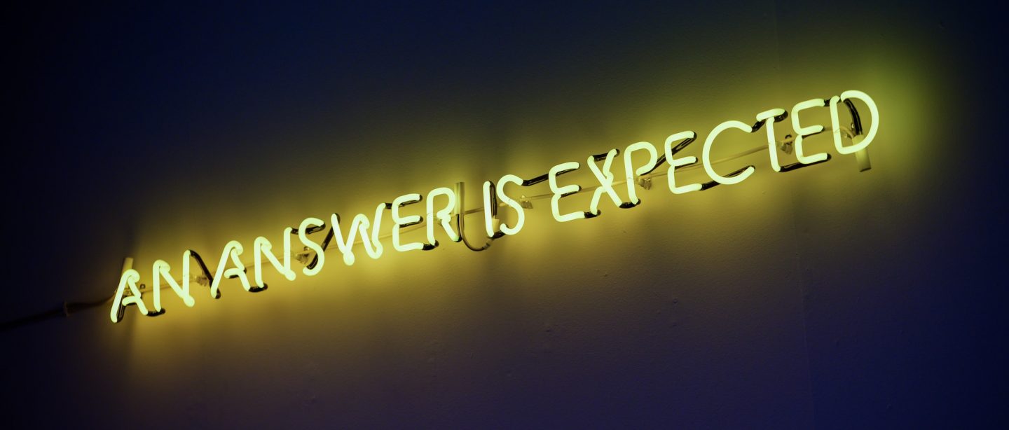 A yellow neon sign that says AN ANSWER IS EXPECTED
