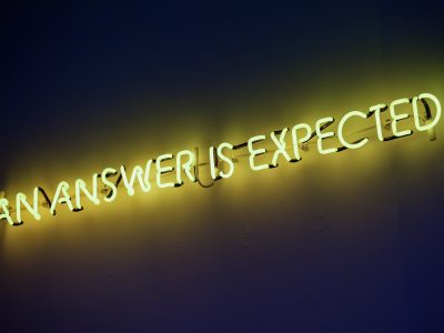 A yellow neon sign that says AN ANSWER IS EXPECTED