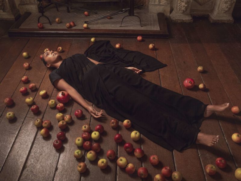A work of art in the Foreign Commonwealth & Development Office; a woman in black lies on a wooden floor surrounded by apples