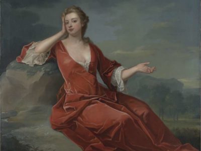 A young woman reclines in the green and grey grounds of an impressive estate in a red dress